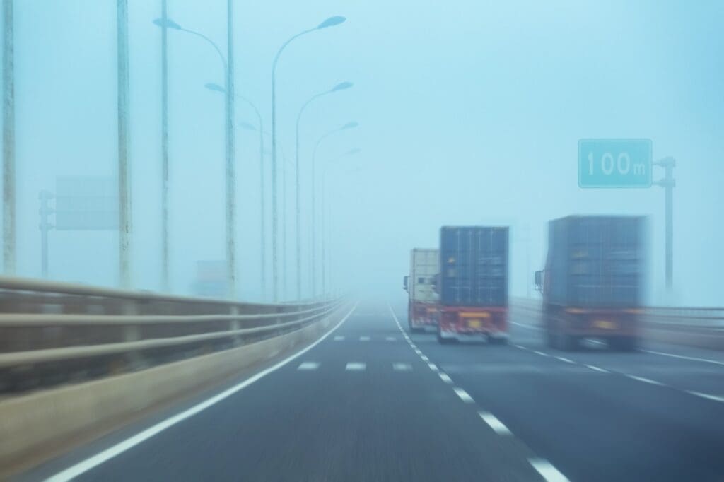 A row of trucks barely visible through a dense fog, symbolizing the obscured reality of sexual abuse within the trucking industry.