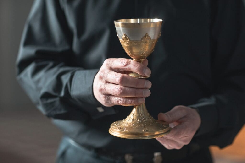 Priest in religious attire holding a ceremonial cup, symbolizing the trust and authority in religious institutions under scrutiny in clergy sexual abuse cases.