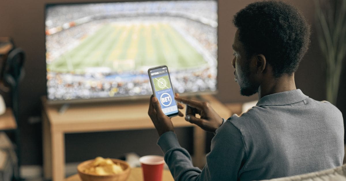 Person holding a smartphone with a sports betting app, illustrating the financial impact of gambling addiction.