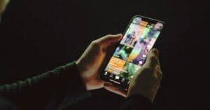 Hands holding a smartphone in a dark room showing a colorful, continuous vertical video interface, illustrating algorithmic compulsion.